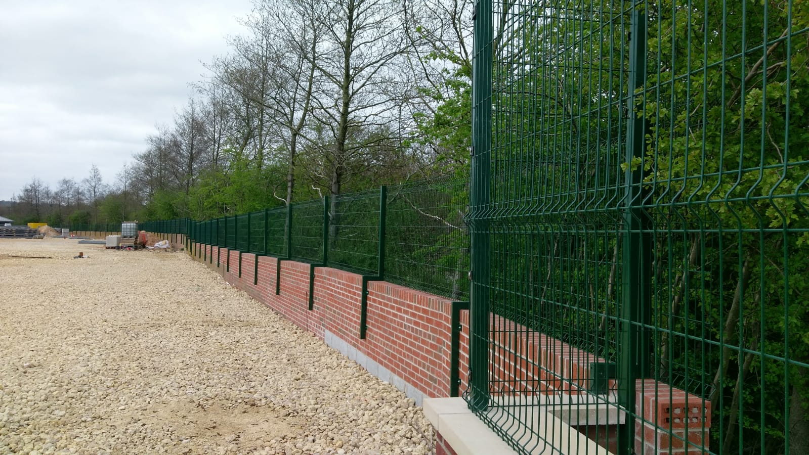 Green V-Mesh Fencing barrier secured atop red brick wall